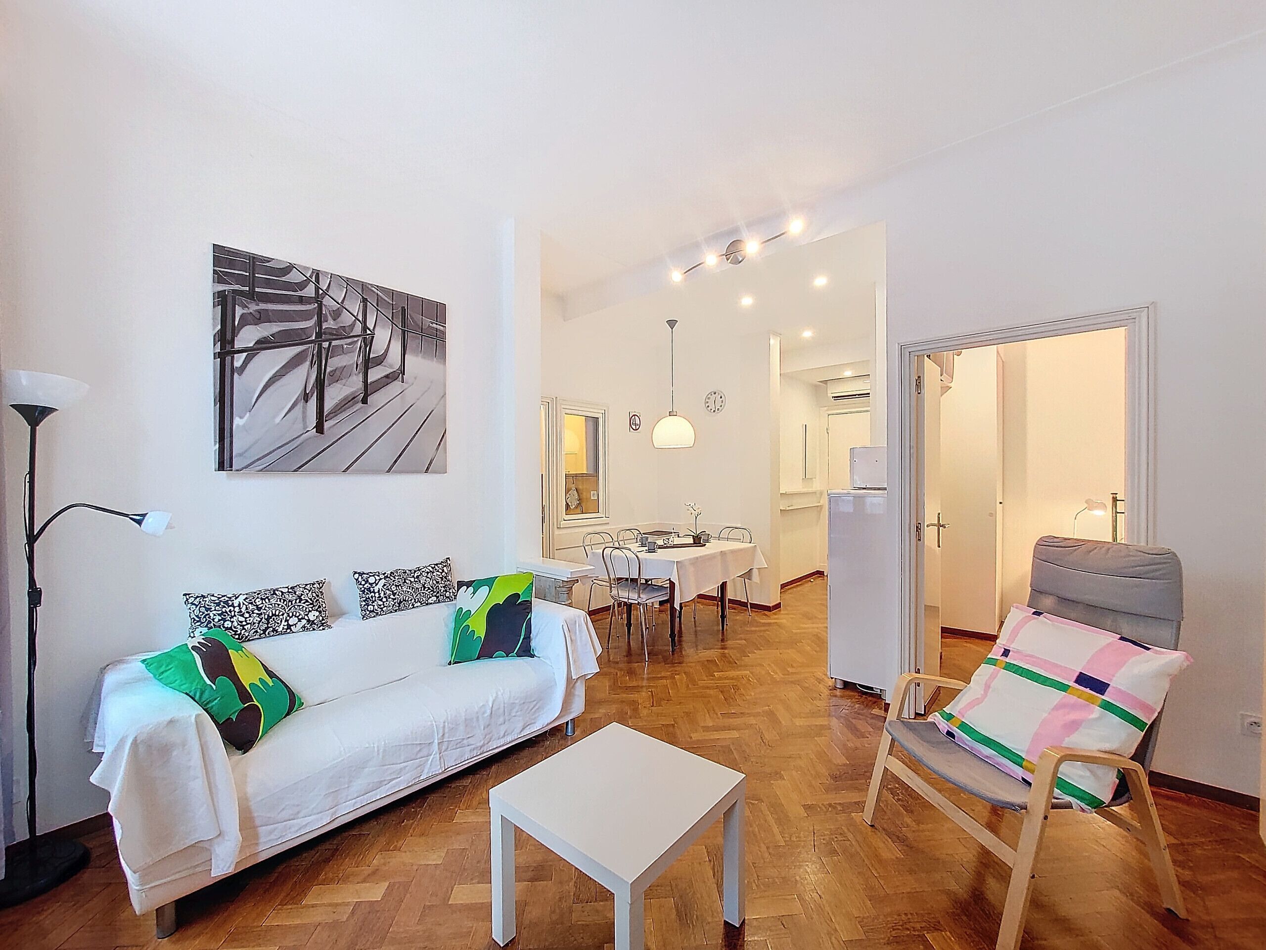 Una sala de estar moderna con un sofá blanco, una mesa de comedor y una cocina al fondo.