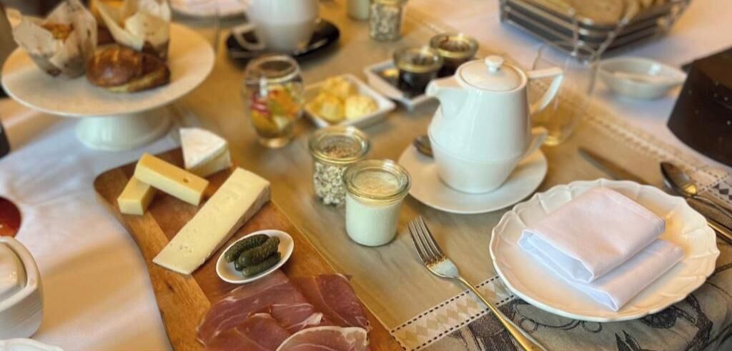A breakfast setting with various food items, including cheese, meats, and condiments on a wooden board.