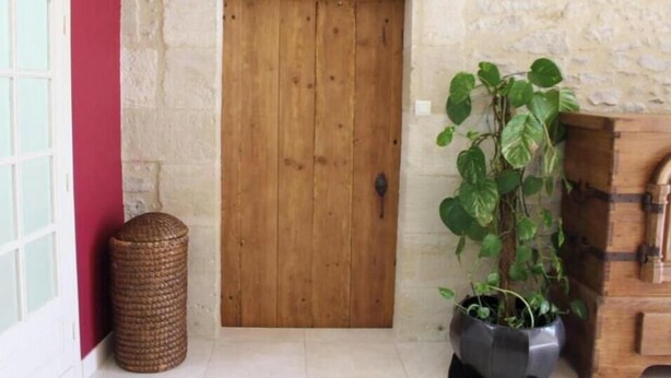 Una porta de fusta al costat d'una paret de pedra, una planta en test i una cistella de vimet.