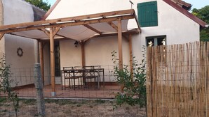 A covered patio area with a table and chairs, a wooden pergola, and a fenced garden.