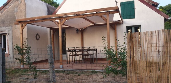 A covered patio area with a table and chairs, a wooden pergola, and a fenced garden.