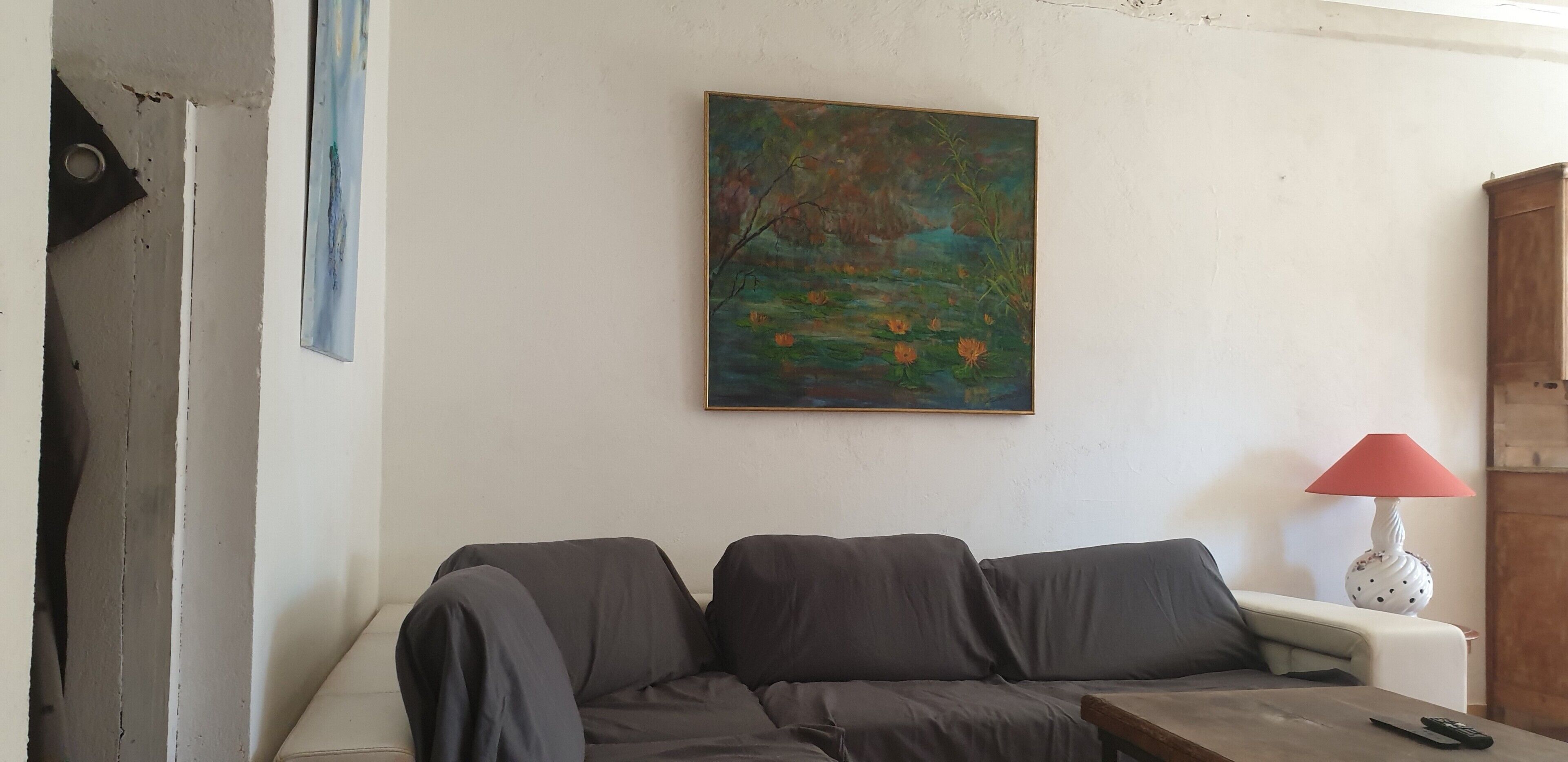 Una sala de estar con un sofá, un cuadro, una lámpara y una puerta visible solo en parte.