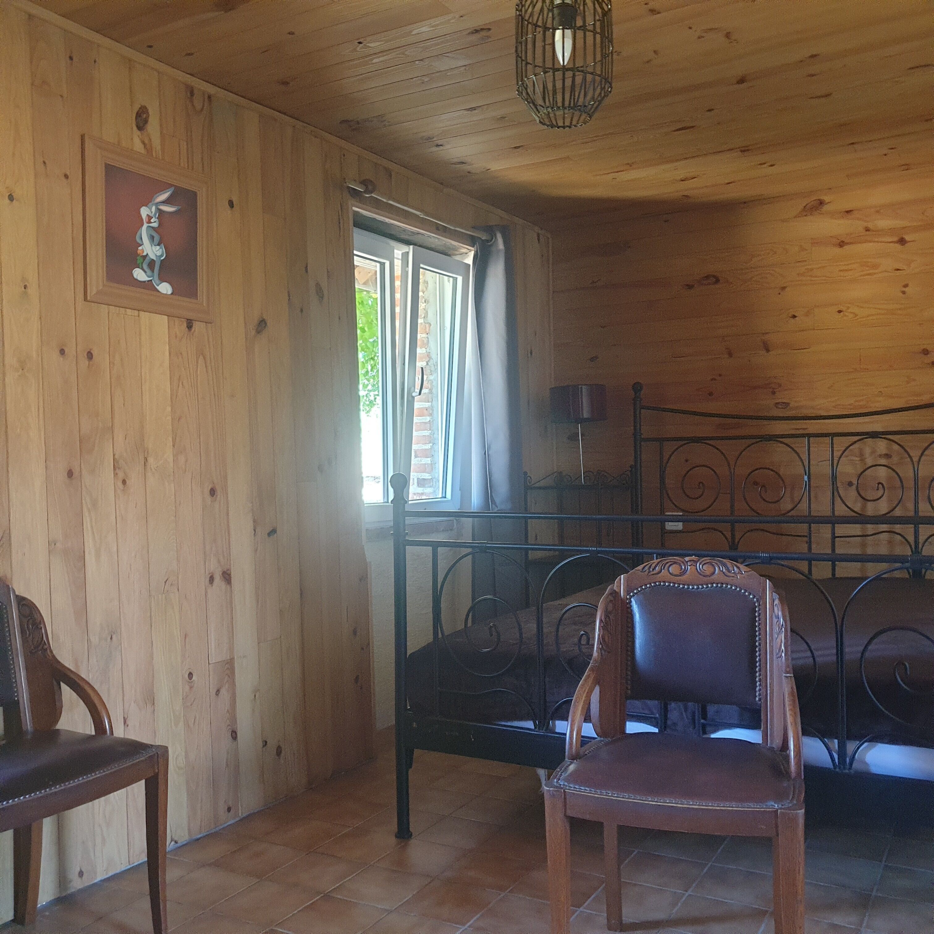 Une pièce en bois avec un lit, une chaise, un tableau accroché au mur et une fenêtre.
