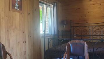 Une pièce en bois avec un lit, une chaise, un tableau accroché au mur et une fenêtre.