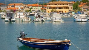 Un puerto deportivo con barcos amarrados, un edificio con tejados de tejas rojas y montañas al fondo.