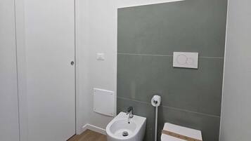 A small bathroom with a bidet, toilet, and a white door.