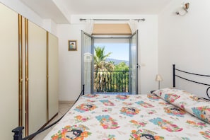 Une chambre à coucher comprenant un lit, une armoire, un balcon avec vue et une petite table avec une lampe.