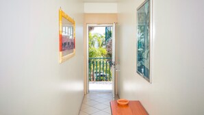 Un estrecho pasillo con una puerta que da a un balcón con baranda verde y plantas.