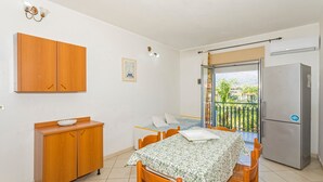 Habitación pequeña con cama, una mesita, un armario de madera, un refrigerador y un balcón con vistas.