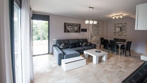 A modern living room with a grey sectional sofa, a white coffee table, and a dining area with a table and chairs. - Dream Villa in Cap Salou - Pool & Beach Paradise (Salou)
