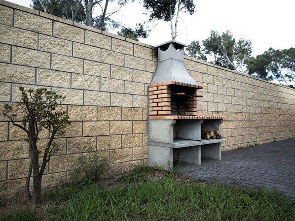 A brick-built outdoor oven against a stone wall, with a small tree and grass in the foreground. - Dream Villa in Cap Salou - Pool & Beach Paradise (Salou)