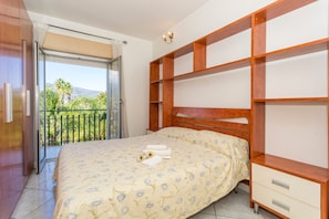 Une chambre à coucher comprenant un lit, une armoire en bois, un balcon avec vue et un luminaire au plafond.