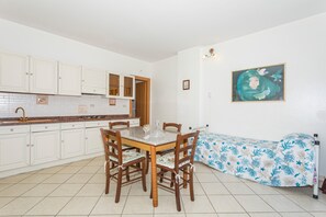 A kitchen with white cabinets, a dining table with chairs, and a bed with a floral bedspread.