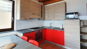 Une cuisine moderne avec des poutres en bois, des armoires rouges, une cuisinière à gaz et un four à micro-ondes.