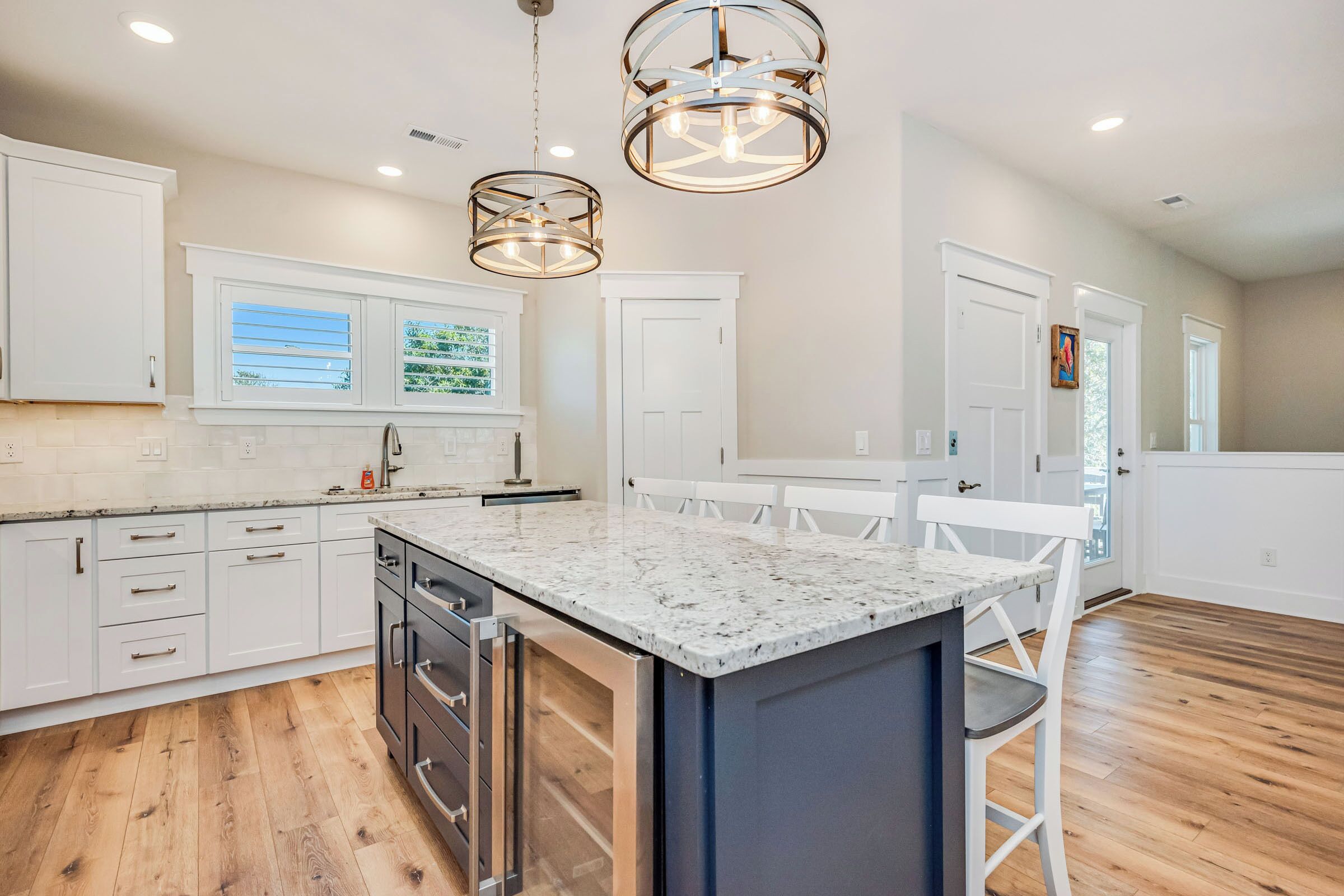 A modern kitchen with white cabinets, a granite countertop, and pendant lighting.