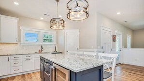 Une cuisine moderne avec des meubles blancs, un plan de travail en granit et des luminaires suspendus.