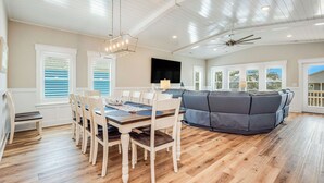 Une pièce spacieuse comprenant une table à manger, des chaises, un canapé gris et un ventilateur de plafond.