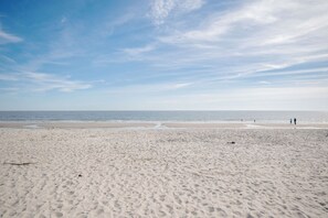 Una extensa playa de arena con cielo despejado y mar tranquilo.