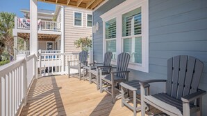 Une terrasse en bois avec des chaises Adirondack et une table, un balcon avec des balustrades, et un bâtiment avec un revêtement bleu et des bordures blanches.