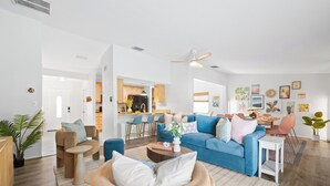 A spacious living room with a blue sofa, a round wooden chair, and a coffee table. There is a kitchen area in the background with wooden cabinets and a dining table. - Family Resort Near Beaches, with Heated Pool, Hot Tub, Mini Golf & Games (Bradenton)