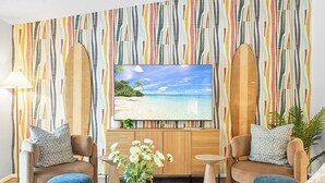 A living room with a large TV on the wall, two armchairs, a coffee table, and a plant. - Family Resort Near Beaches, with Heated Pool, Hot Tub, Mini Golf & Games (Bradenton)