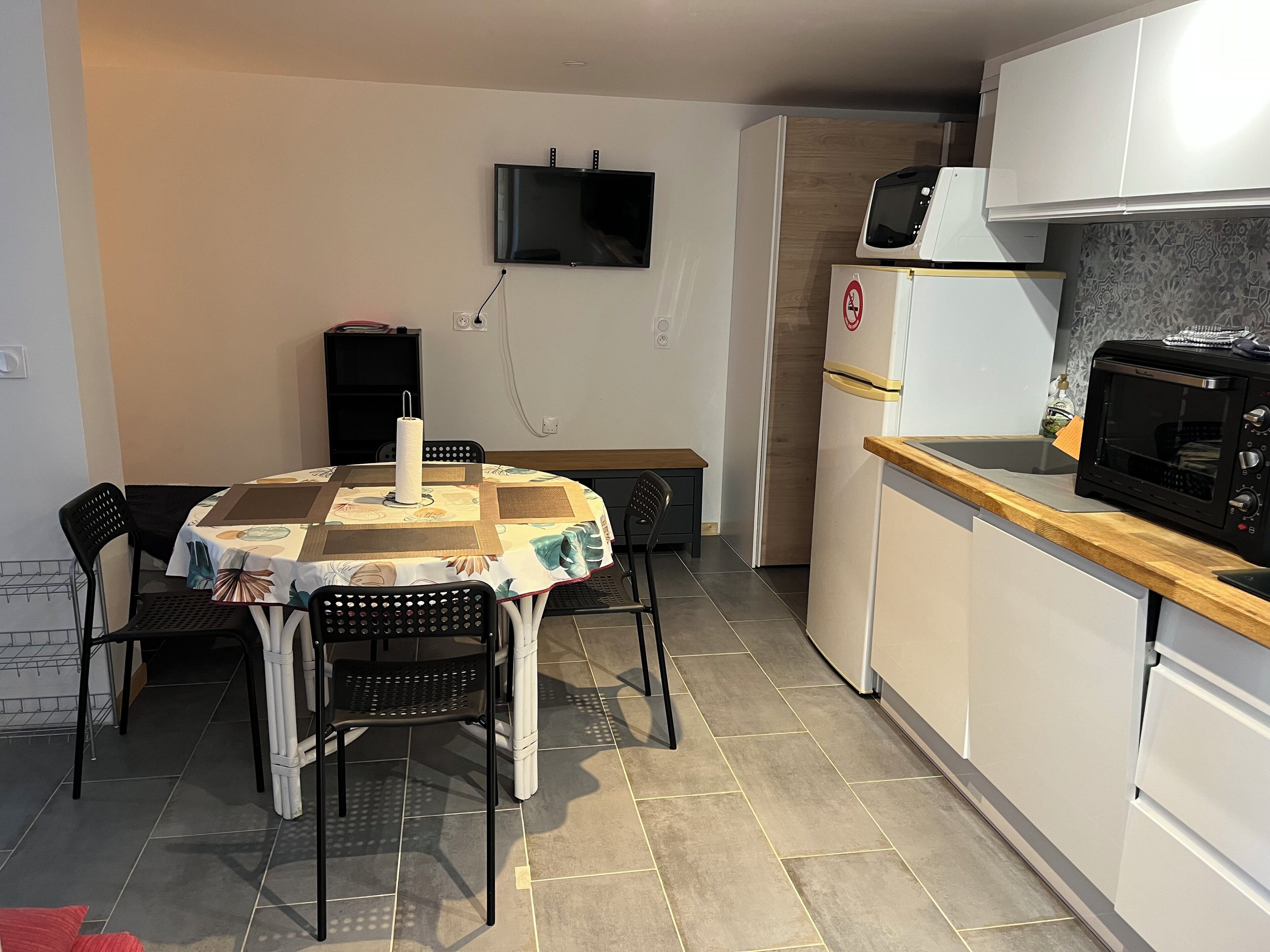 Uma cozinha compacta com mesa de jantar, cadeiras, televisão, micro-ondas e frigorífico.