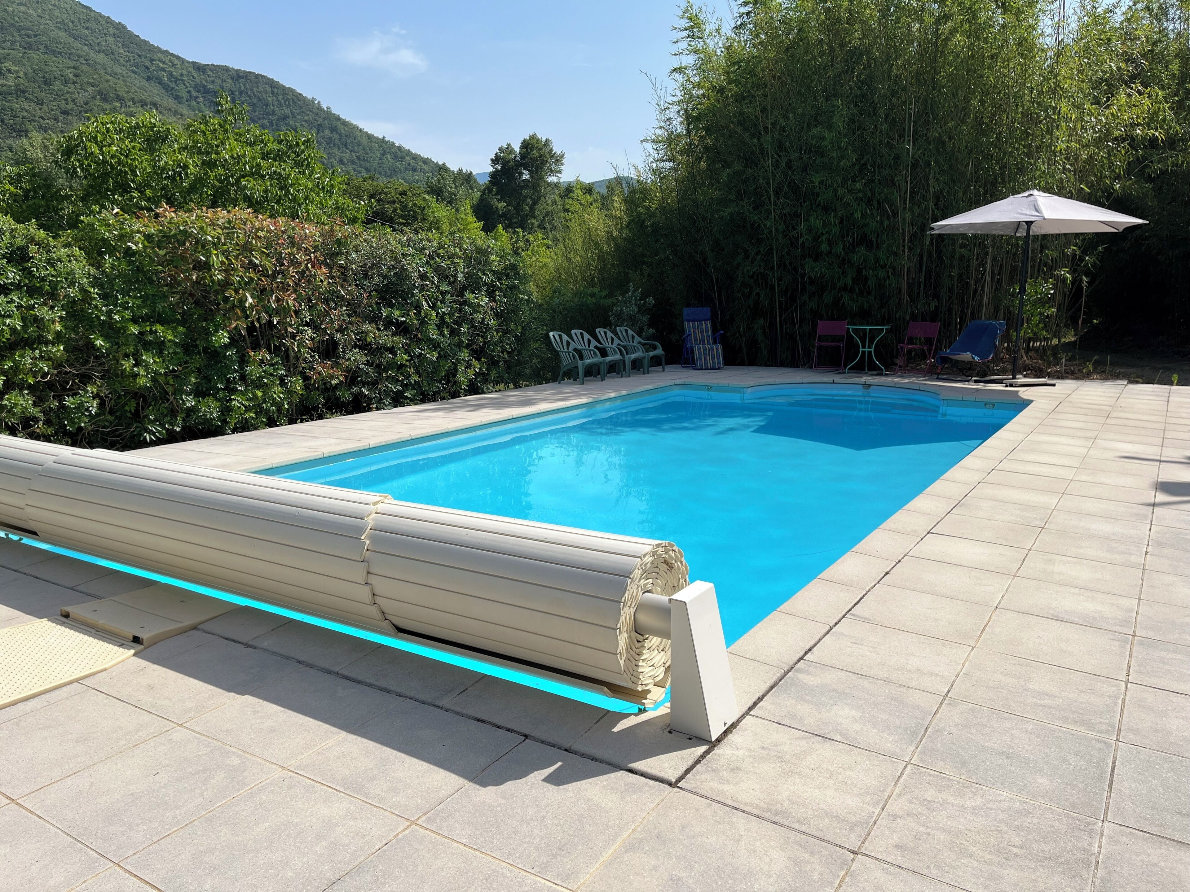 Una piscina rettangolare con bordo piastrellato, immersa nel verde e circondata da colline.