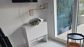 A modern living room with a flat-screen TV mounted on the wall, a white console table with a decorative item, a green sofa, and a small round table with a basket.