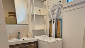 A compact laundry room with a washing machine, a sink, and a mirror.