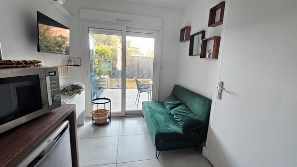 A compact living space with a kitchenette, a green sofa, a dining area with a chair, and a sliding glass door leading to a patio.