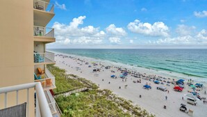 A beach with a view of the ocean, a building with balconies, and a clear sky.