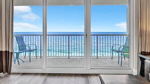 A balcony with a view of the ocean, two chairs, and a table.
