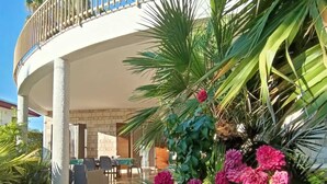 A circular building with a balcony, surrounded by lush greenery and flowering plants.