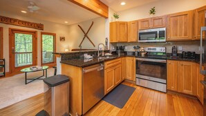 A modern kitchen with wooden cabinets, stainless steel appliances, and a large window with a view of trees.