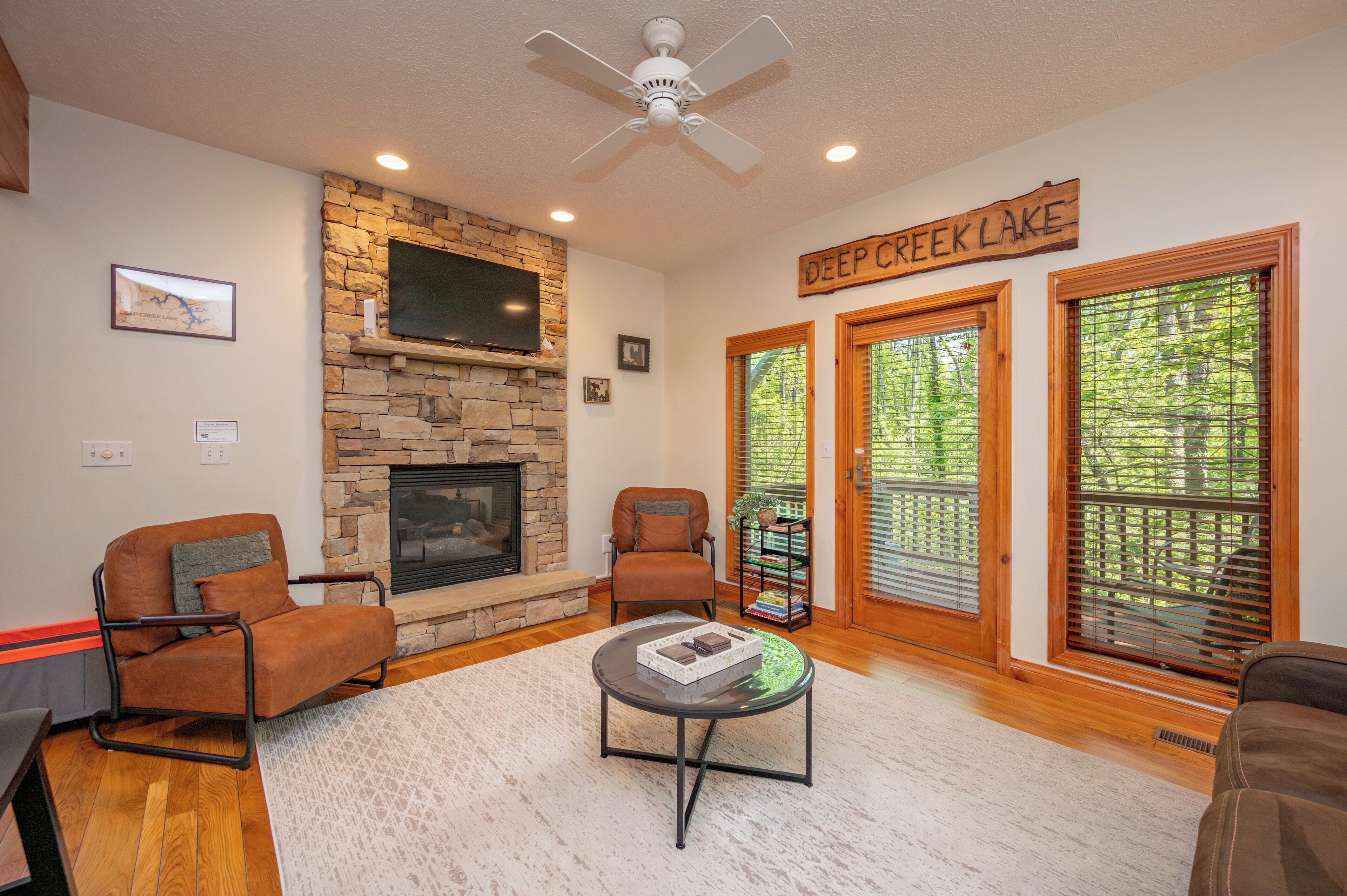 A cozy living room with a stone fireplace, two leather armchairs, a coffee table, and a sign reading "Deep Creek Lake".