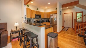 A modern kitchen with wooden cabinets, a central island with stools, a microwave, and a refrigerator.