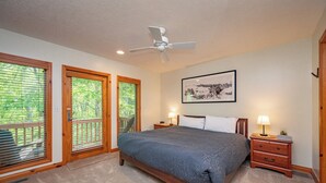 A bedroom with a bed, two bedside tables with lamps, a ceiling fan, and a framed picture on the wall.