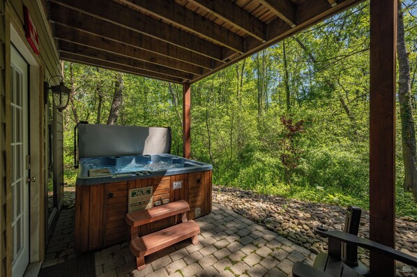 A hot tub under a wooden pergola with a stone pathway leading to it, surrounded by a forest.