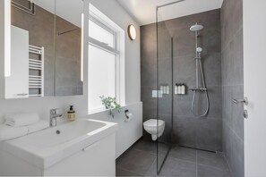 Un baño moderno con ducha de vidrio, un lavabo blanco y un espejo grande.