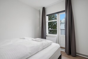 Un dormitorio con una cama grande, una ventana con cortinas y vistas a una casa.