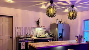 A modern kitchen with a central island, bar stools, a refrigerator, and a unique spherical pendant light. - Modern Stay By the Falls – Renovated & Walkable! (Niagara Falls)