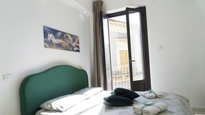 A bedroom with a green headboard, a bed with a floral bedspread, two pillows, and two towels on the bed. - [ Martiry Suite Apartment ] + Self Check-in Late (Catania)