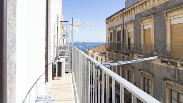 A balcony with a view of the sea, a metal railing, and a building with classical architecture. - [ Martiry Suite Apartment ] + Self Check-in Late (Catania)