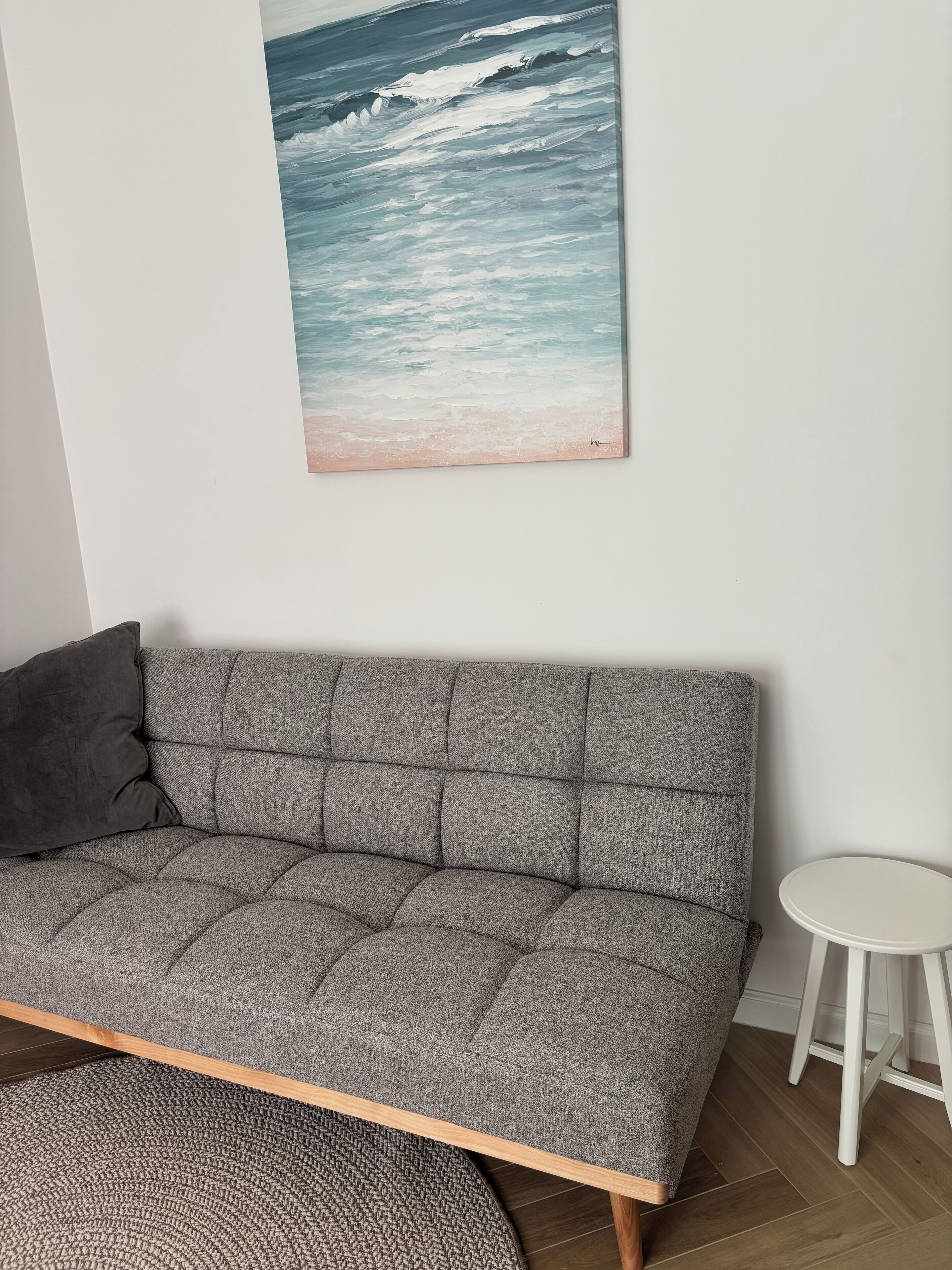 A grey sofa with a dark cushion, a small white stool, and a patterned rug.