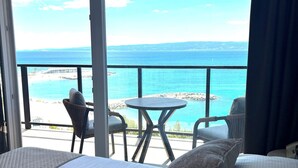 A hotel room with a bed, pillows, and a view of the sea and beach through large windows. - Stella's beachfront aparthotel (Split)