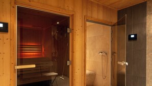 A sauna with a bench and a glass door leading to a shower area with a tiled wall and a control panel. - Entire chalet with indoor pool jacuzzi sauna steam room (Taninges)
