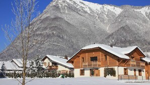 A wooden chalet with a balcony, surrounded by snow-covered trees and a mountain backdrop. - Entire chalet with indoor pool jacuzzi sauna steam room (Taninges)