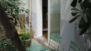 A small, enclosed outdoor space with a green chair, a wicker basket with plants, and a door leading to an interior room. - Puccini- un bel dì (Cagliari)
