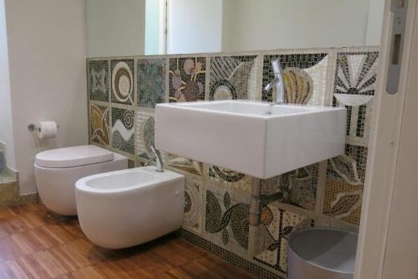 A bathroom with a white sink, two toilets, and a tiled backsplash with a floral pattern. - Puccini- un bel dì (Cagliari)