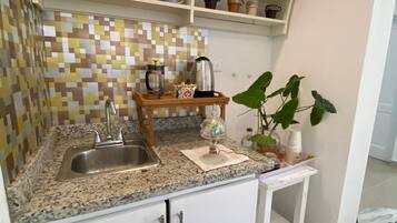 A compact kitchen with a granite countertop, a coffee maker, a kettle, and a small shelf with coffee mugs.